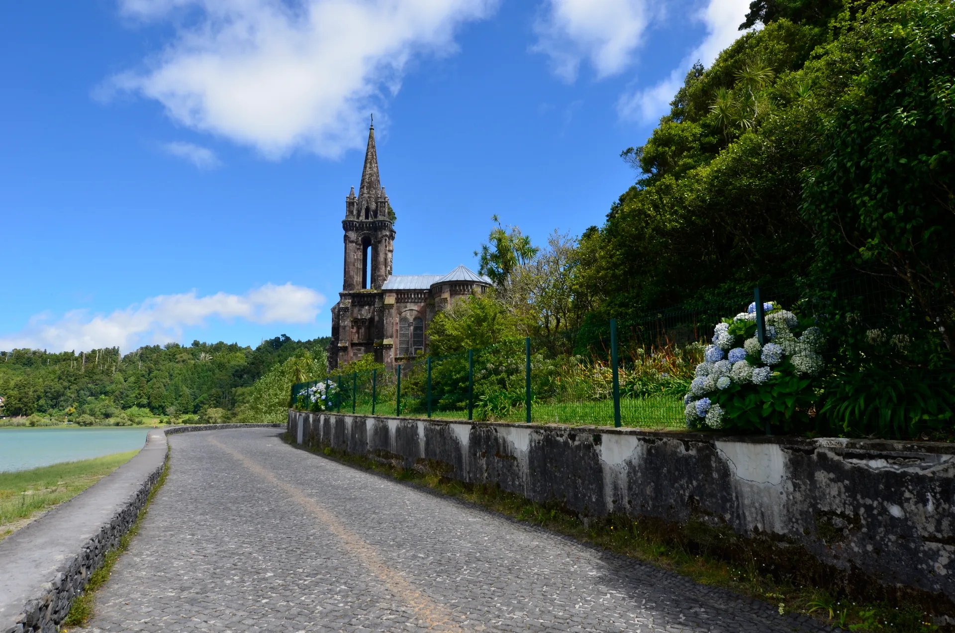 Capela de torre pontiaguda junto a uma estrada de pedra, com hortênsias, na margem da Lagoa das Furnas, nos Açores