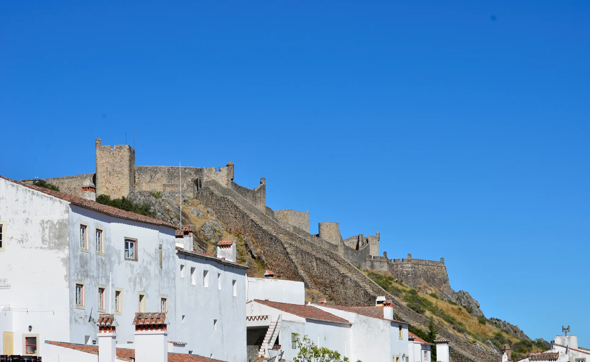 Casas brancas da vila e as muralhas do Castelo de Marvão no alto da serra, sob céu azul, em Portugal