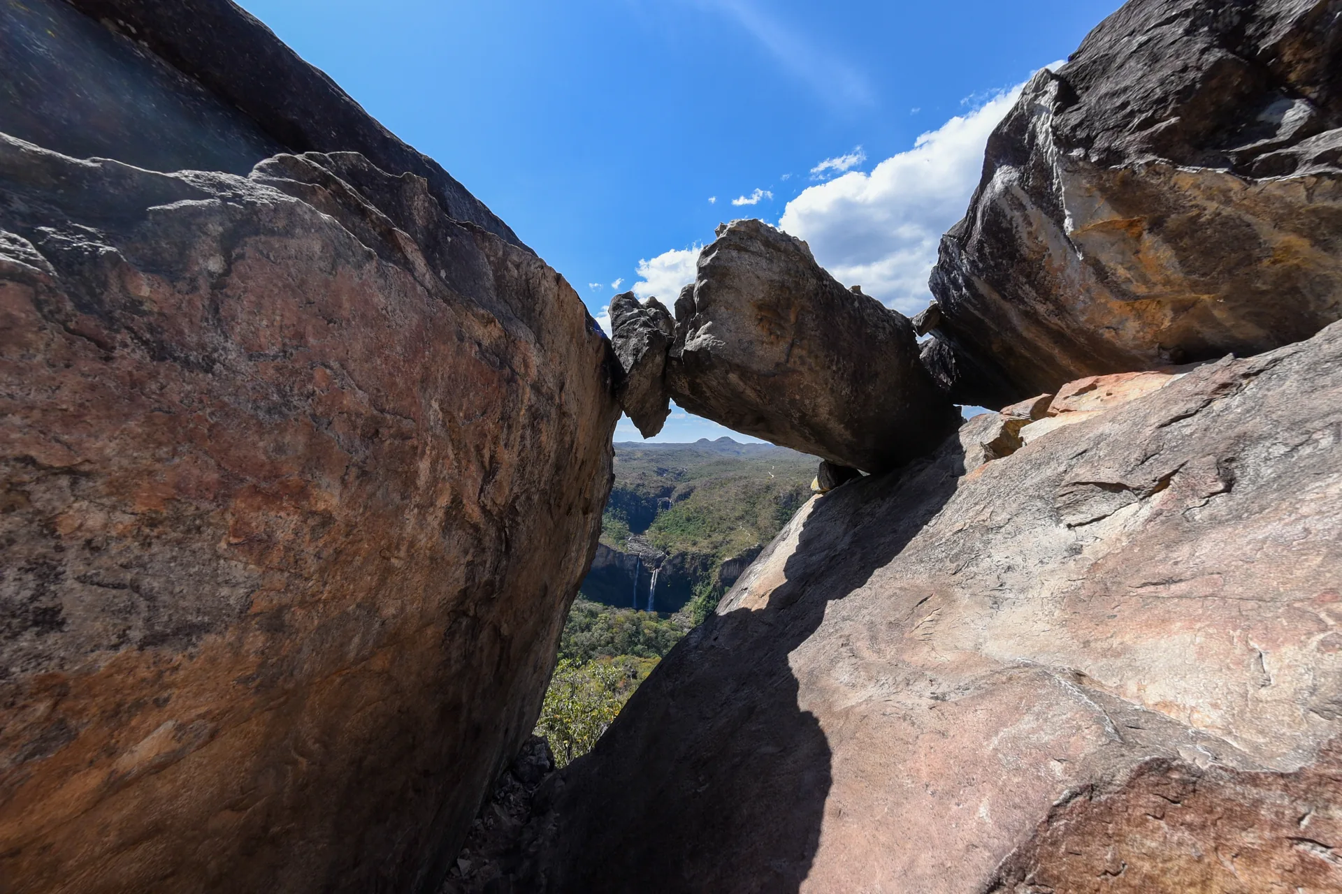 Pedra encaixada entre dois rochedos formando uma janela para o vale e a cachoeira, na Chapada dos Veadeiros