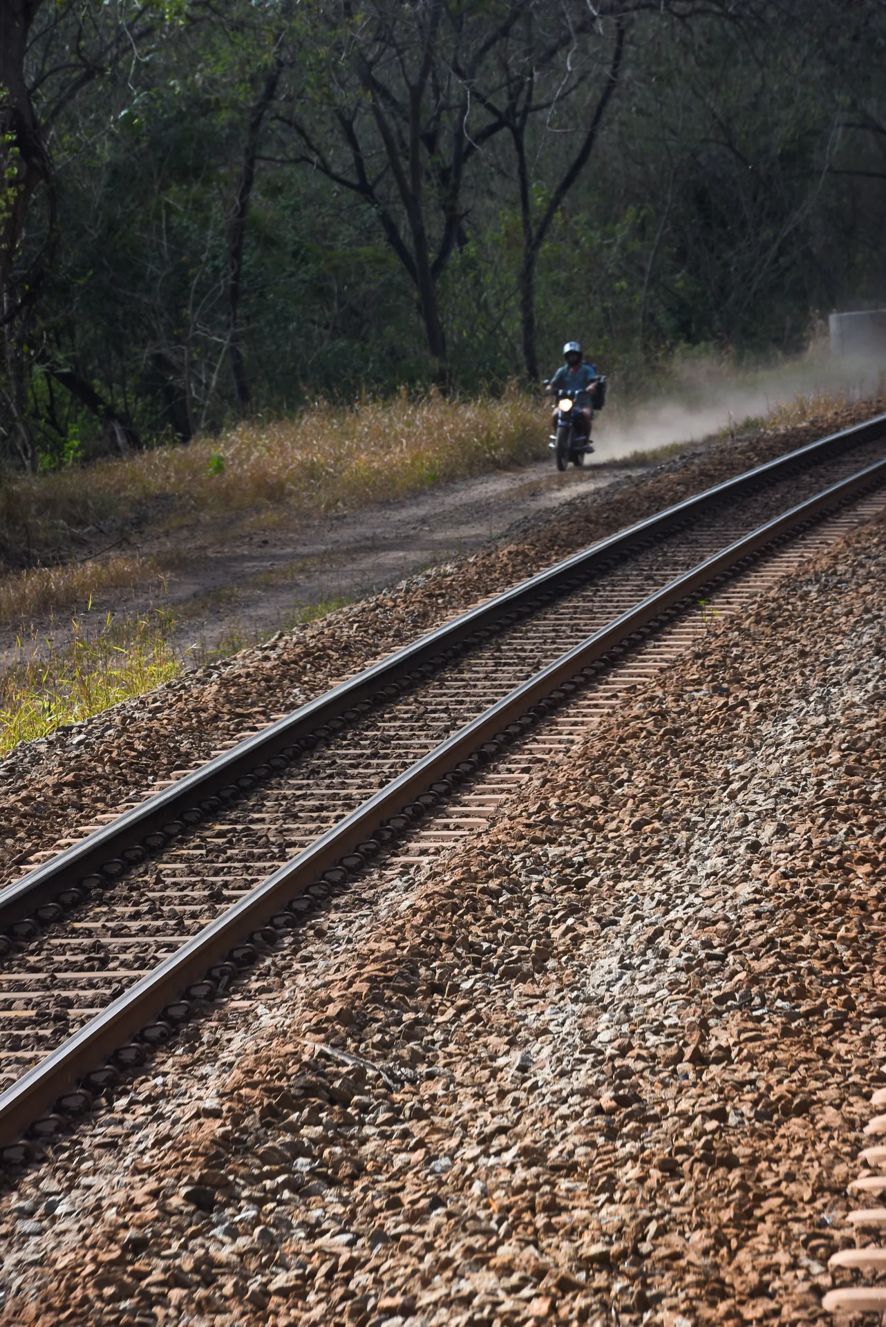 Motociclista numa estrada de terra ao lado dos trilhos da Estrada de Ferro Vitória a Minas