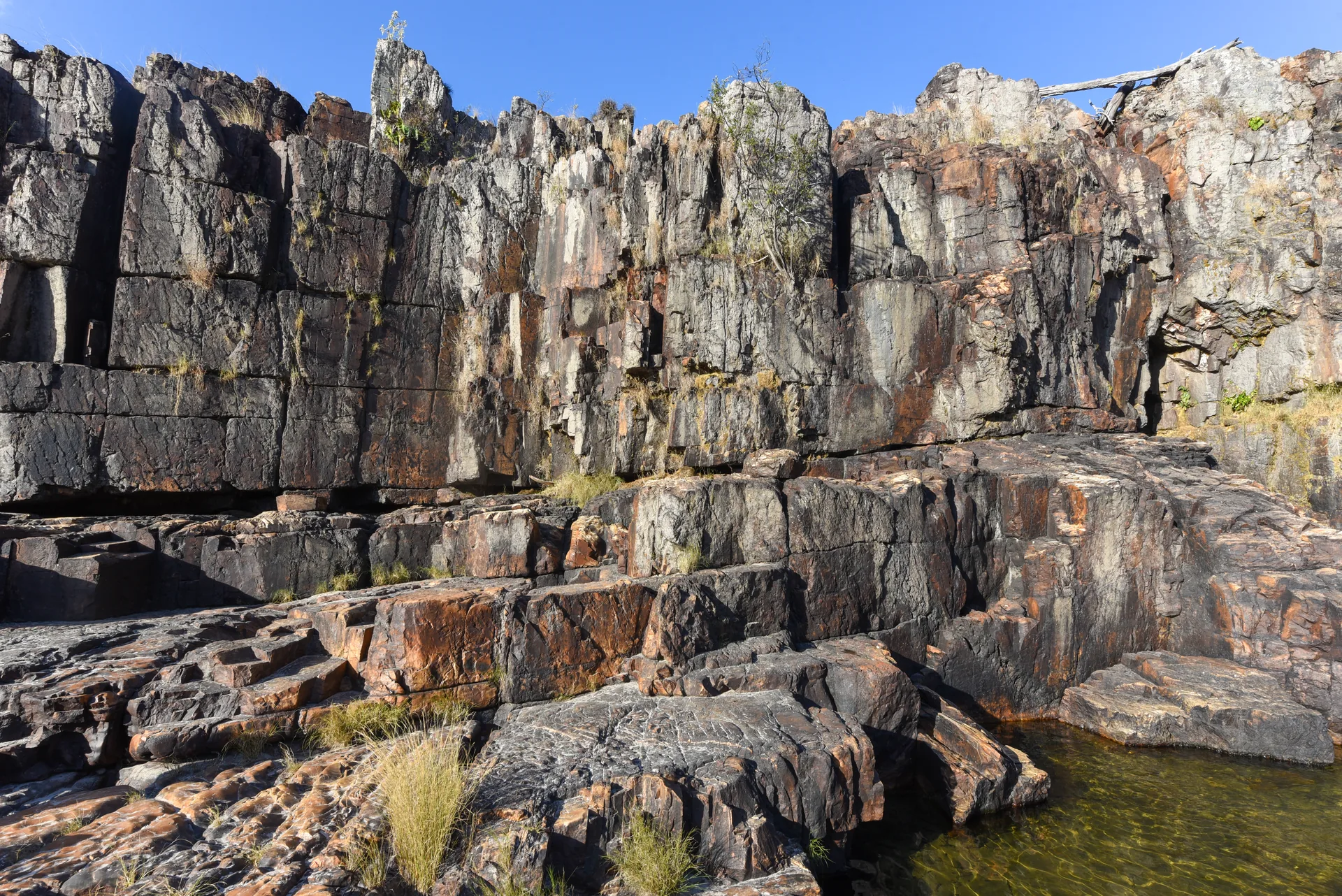 Paredões de pedra escura e avermelhada sobre um poço, na Cachoeira da Muralha, na Chapada dos Veadeiros