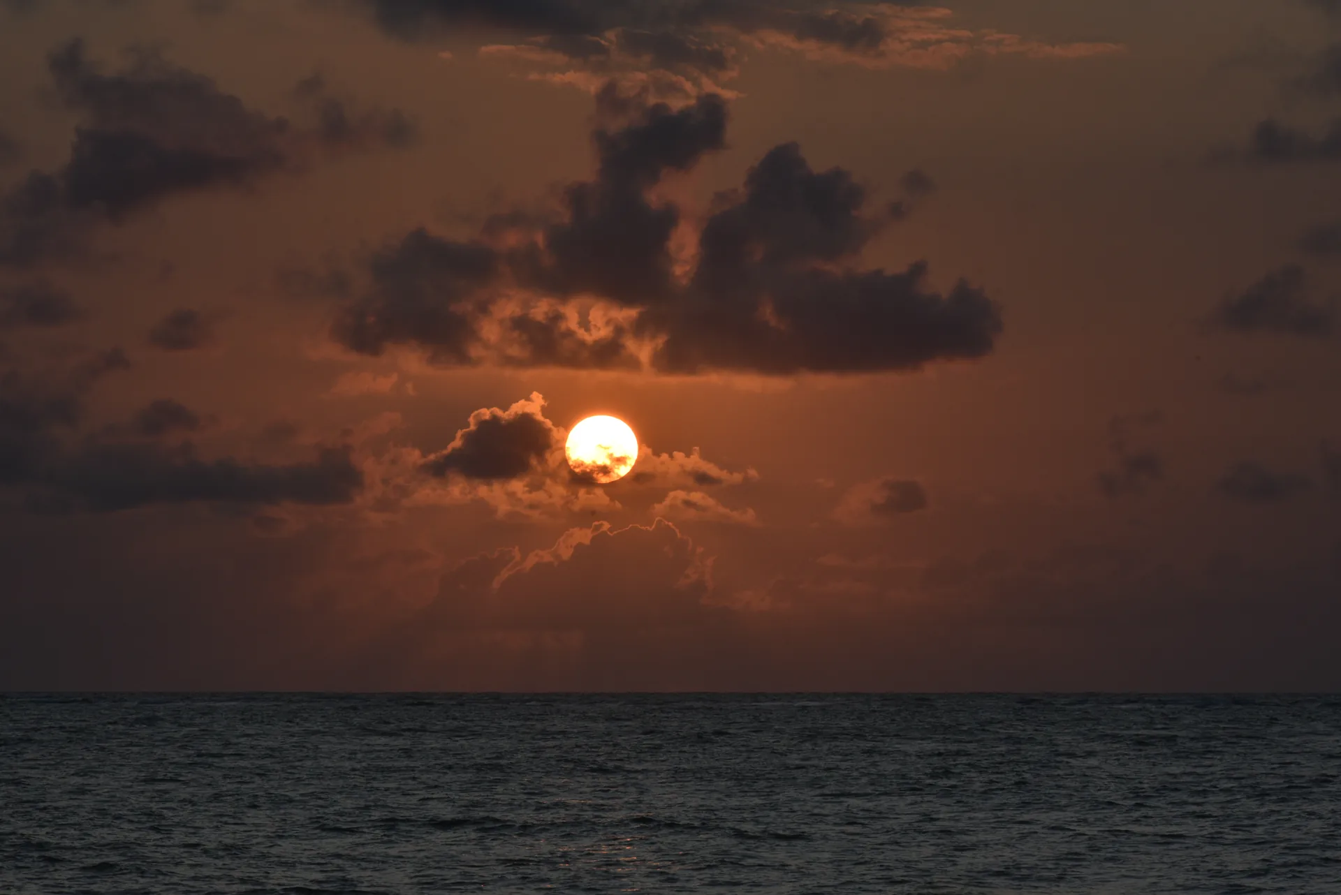 Sol nascendo entre nuvens escuras sobre o mar, em tons de laranja, em Japaratinga, Alagoas