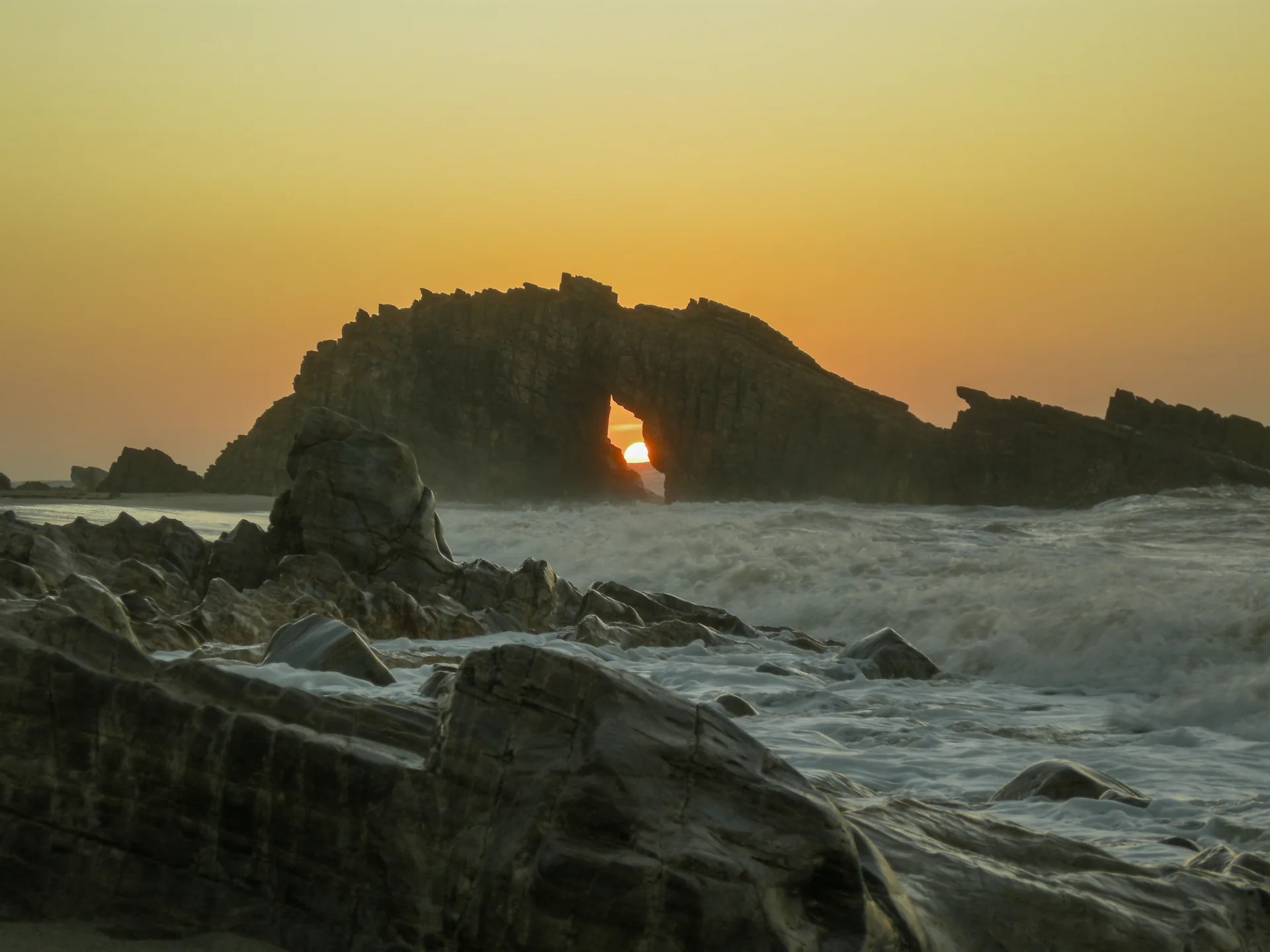 Sol no vão da Pedra Furada, arco de rocha diante do mar agitado, em Jericoacoara, no Ceará