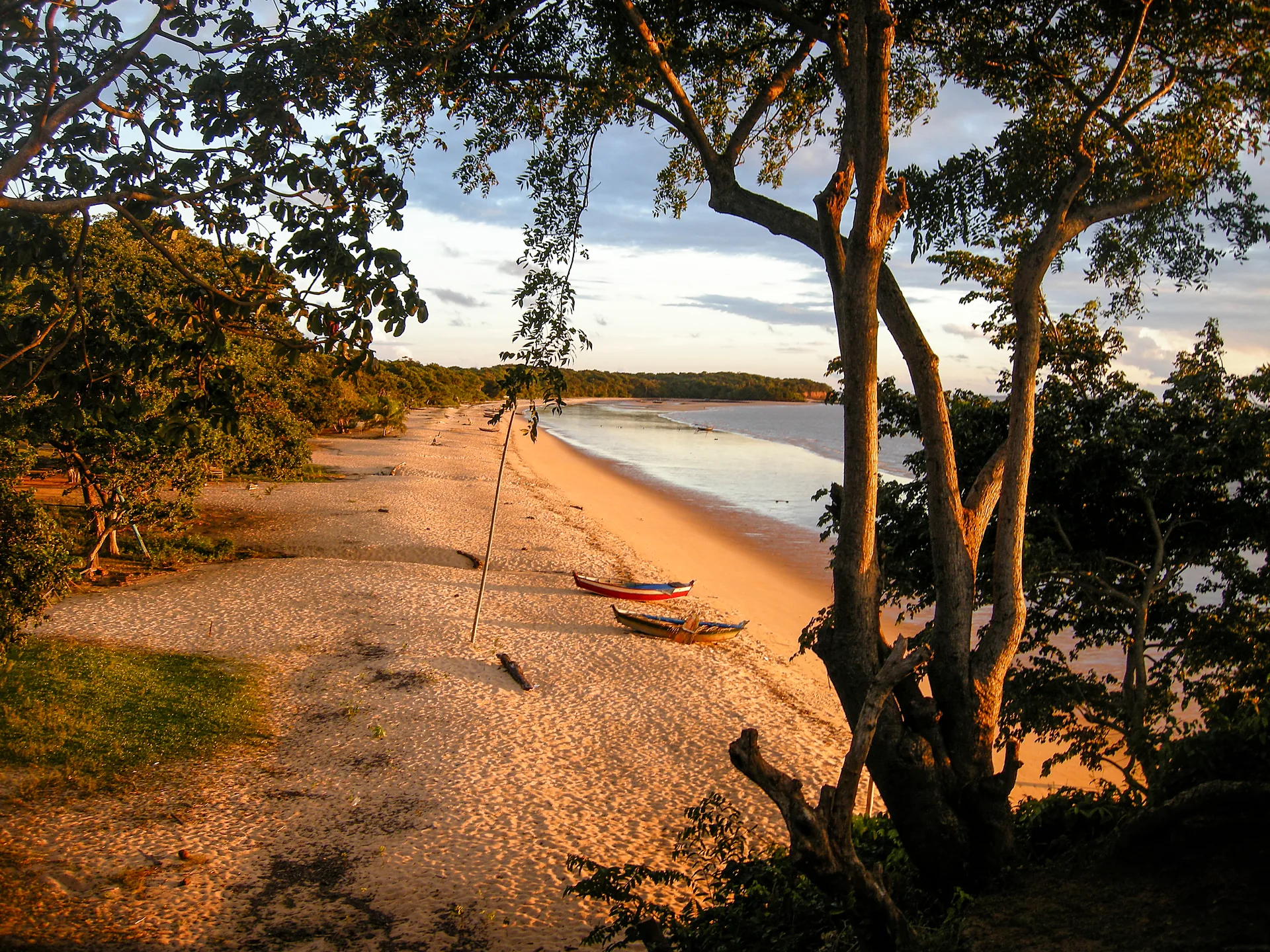 Faixa de areia curva com barcos na beira d'água, emoldurada por árvores, na Praia de Joanes, na Ilha de Marajó